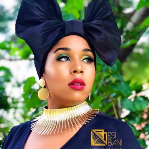 May include: A woman wearing a black head wrap with a large bow, gold earrings, and a gold choker necklace. The text "ESI BANI HANDCRAFTED www.EBODESIGNPLAZA.COM" is visible in the bottom right corner of the image.