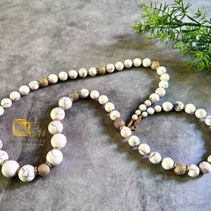 May include: A white and gold beaded necklace and bracelet set. The beads are large and round, with a marbled pattern. The necklace is longer than the bracelet, and both have gold accents.
