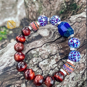 May include: A bracelet with red tiger's eye beads, blue and white patterned beads, and a large blue lapis lazuli bead. The bracelet is on a wooden surface.