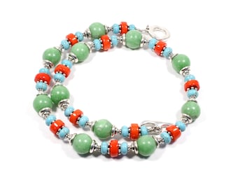May include: A green, turquoise, and orange beaded necklace with silver accents. The necklace is made of round beads and has a silver clasp.