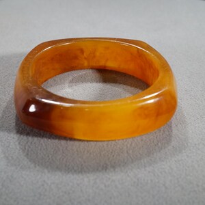 May include: A square-shaped amber-colored plastic bangle bracelet.