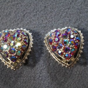May include: A pair of silver heart-shaped earrings with iridescent red, purple, and blue rhinestones.