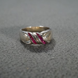 May include: A silver ring with a twisted band design and three rows of red ruby stones.