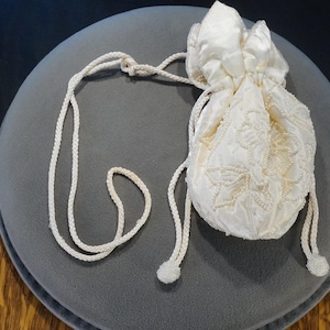 May include: A white satin drawstring bag with a beaded design and a white cord.