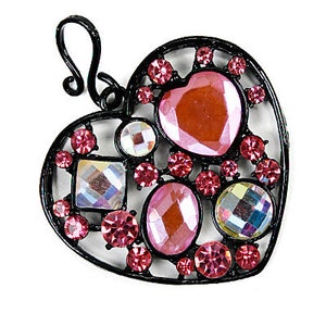 May include: A heart-shaped pendant with a black metal frame. The pendant is adorned with various pink and iridescent gemstones of different shapes and sizes. A loop is at the top for hanging.
