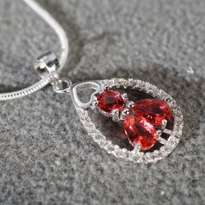 May include: A silver necklace with a pendant featuring three red teardrop-shaped stones surrounded by smaller clear stones.