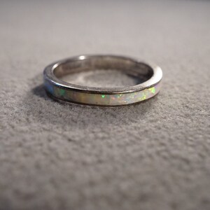 May include: A silver band ring with a thin white opal inlay.