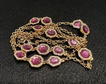 May include: A gold chain necklace with multiple strands and large, faceted, purple gemstones. The gemstones are set in gold and have a sparkly finish.