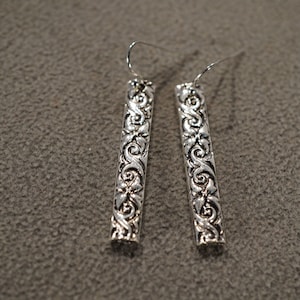 May include: A pair of silver dangle earrings with a floral design. The earrings are long and narrow, with a delicate hook closure.