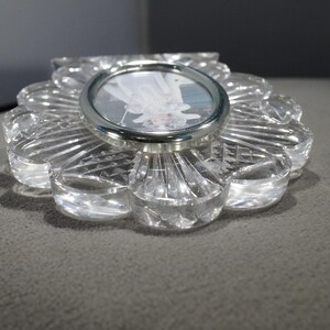 May include: A clear glass picture frame with a flower-shaped design. The frame has a silver metal rim around the photo opening.