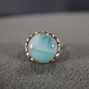 May include: A silver ring with a round, blue and white gemstone set in a gold-toned bezel.