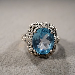 May include: A silver ring with a large oval blue topaz gemstone set in a filigree design.