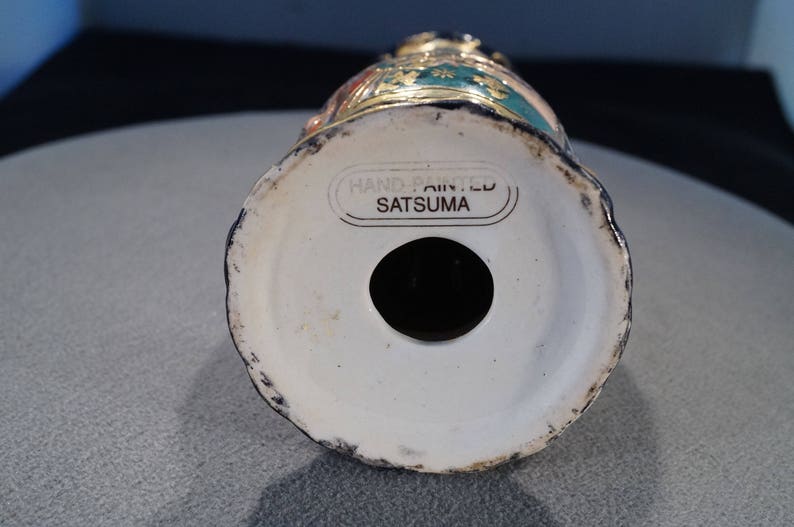 May include: The base of a hand-painted Satsuma ceramic vase featuring a gold and green floral design. The vase is marked "Hand Painted Satsuma" on the underside.