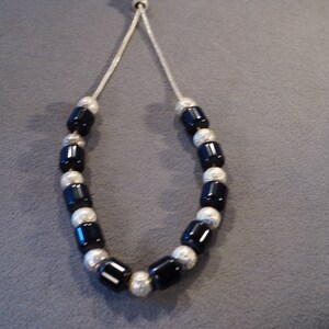May include: A black and silver beaded necklace with a silver clasp. The beads are round and have a textured surface.