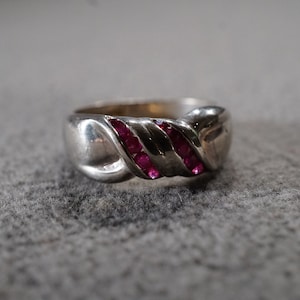 May include: A silver ring with a twisted band design and red ruby stones set into the band.