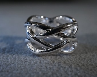 May include: A silver ring with a woven design. The ring is made of a single piece of metal that is twisted and intertwined to create a unique and intricate pattern.