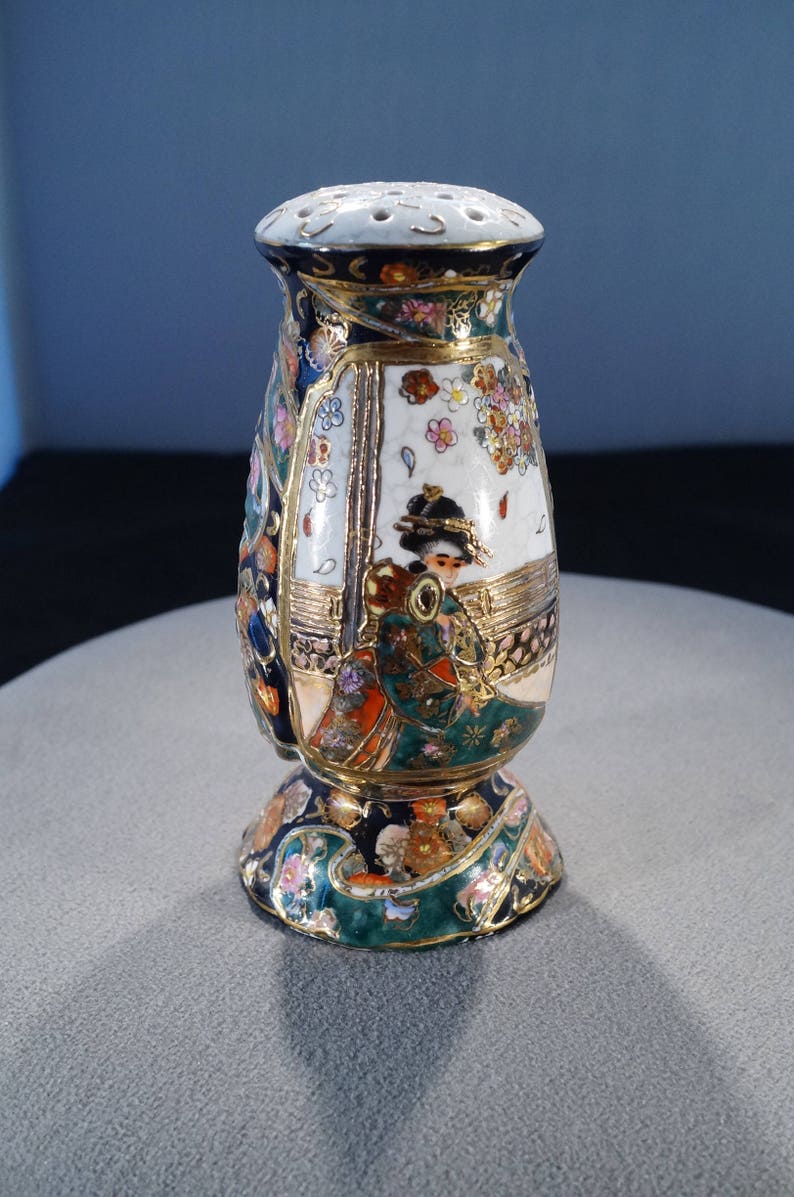 May include: A ceramic bottle stopper with a gold, green, blue and white floral design. The bottle stopper features a woman in a traditional Japanese kimono.