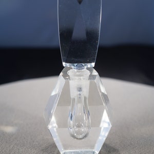 May include: A clear glass bottle with a faceted design and a clear glass stopper. The bottle is empty and has a hexagonal base.