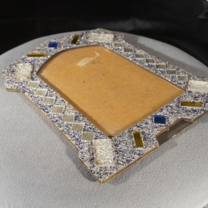 May include: A silver picture frame with a blue and gold mosaic design. The frame is made of cardboard and has a rectangular opening for a photo.