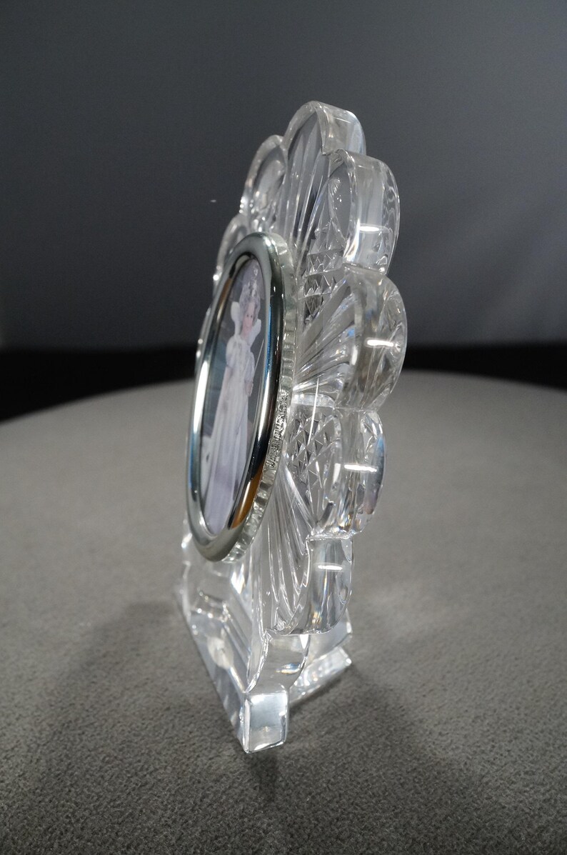 May include: A clear crystal picture frame with a silver-toned oval frame. The frame is shaped like a flower with a stand.