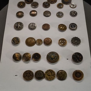 May include: A collection of 27 vintage buttons in various colors and designs, including floral, geometric, and abstract patterns. The buttons are arranged on a white background.