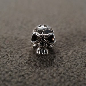 May include: A silver skull charm with detailed features. The skull has a textured surface and is a popular accessory for jewelry making.