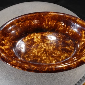 May include: An oval-shaped brown and white ceramic dish with a mottled glaze. The dish is glazed on the inside and outside.