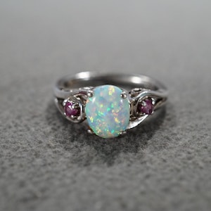 May include: A silver ring with a white opal gemstone and two pink ruby accents.