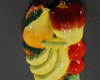 May include: Ceramic fruit wall decor featuring a yellow pear, red apple, yellow bananas, and red cherries. The fruit is painted in a realistic style with vibrant colors.