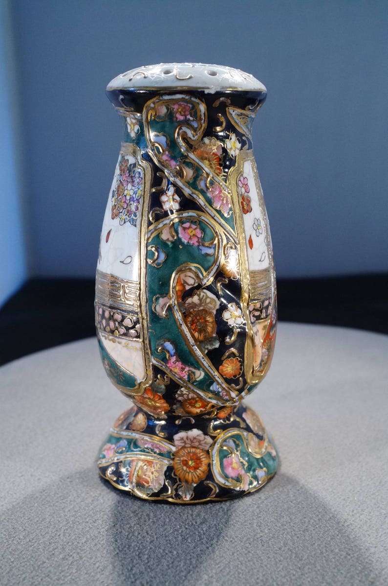 May include: A decorative ceramic vase with a floral pattern in shades of green, gold, pink, and white. The vase has a wide base and a narrow neck.