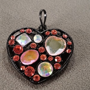 May include: A black metal heart-shaped pendant with a variety of iridescent and pink rhinestones.