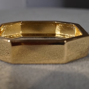 May include: A gold-toned octagonal bangle bracelet. The bracelet is smooth and shiny.