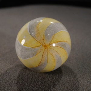 May include: A yellow and gray glass marble with a swirl pattern.