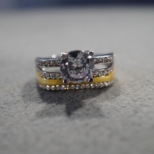 May include: A silver and gold ring with a large, clear, round gemstone surrounded by smaller gemstones.