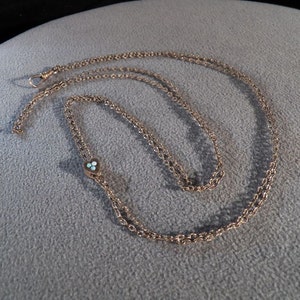 May include: A gold chain necklace with a small heart pendant featuring three light blue stones.