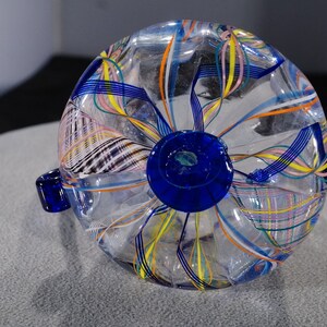 May include: A clear glass vase with a blue base and colorful, swirling lines throughout. The vase is a unique and decorative piece.