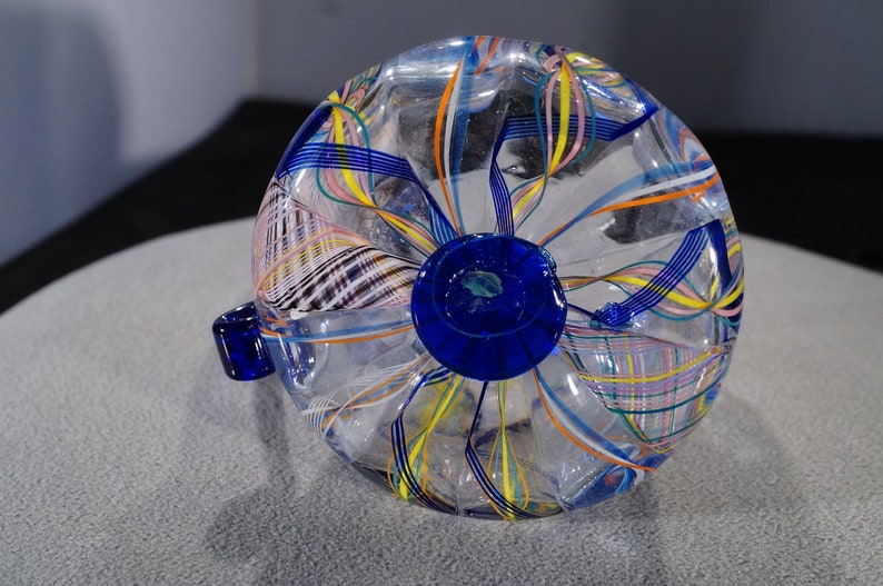 May include: A clear glass vase with a blue base and colorful, swirling lines throughout. The vase is a unique and decorative piece.