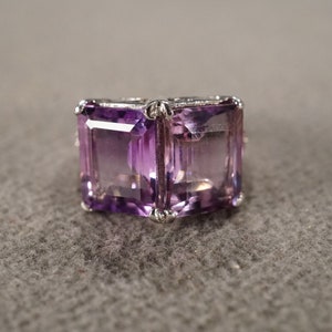 May include: A silver ring with two large, faceted, purple amethyst stones set in a square shape.