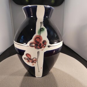 May include: A ceramic vase with a dark blue base and a white vertical stripe design. The vase features red and green floral accents. The vase has a rounded body and a slightly flared rim, suitable for home decor.