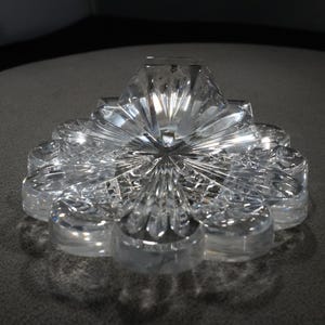 May include: A clear glass flower-shaped dish with a raised center and intricate cut-glass details.