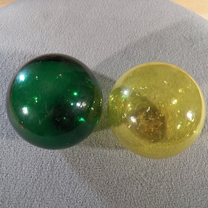 May include: Two glass ornaments, one green and one yellow, with a shiny, reflective surface.