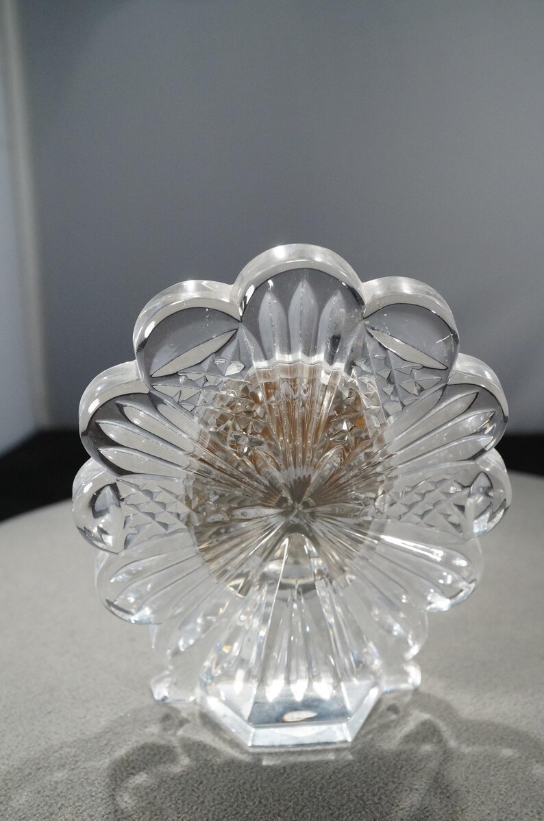 May include: A clear glass picture frame with a flower-shaped design and a crystal base. The frame is decorated with intricate cutouts.