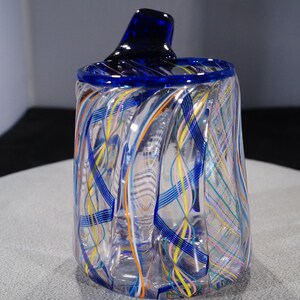 May include: A clear glass vase with a blue rim and a swirling pattern of blue, yellow, orange, and pink lines.