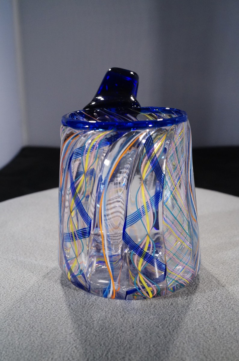 May include: A clear glass vase with a blue rim and a swirling pattern of blue, yellow, orange, and pink lines.