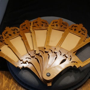 May include: A wooden fan with eight carved frames, each with a rectangular opening. The fan is closed and the frames are arranged in a semi-circle.