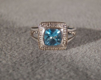 May include: A silver ring with a square blue topaz gemstone surrounded by smaller diamonds.