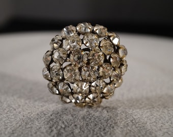 May include: A silver-toned brooch with a cluster of clear rhinestones arranged in a round shape.