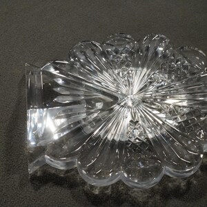 May include: A clear glass decorative dish with a flower-like design. The dish has a scalloped edge and a raised center.