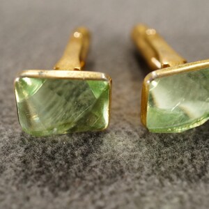 May include: A pair of gold cufflinks with green glass stones. The stones are cut into a square shape with beveled edges.