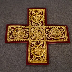 May include: A red velvet cross with gold embroidery. The cross is decorated with intricate floral patterns and has a traditional design.